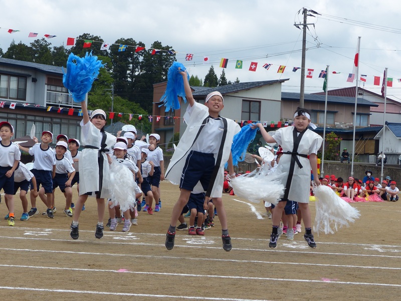 白い法被を着て白と青のポンポンを振りかざして踊る児童たちの写真