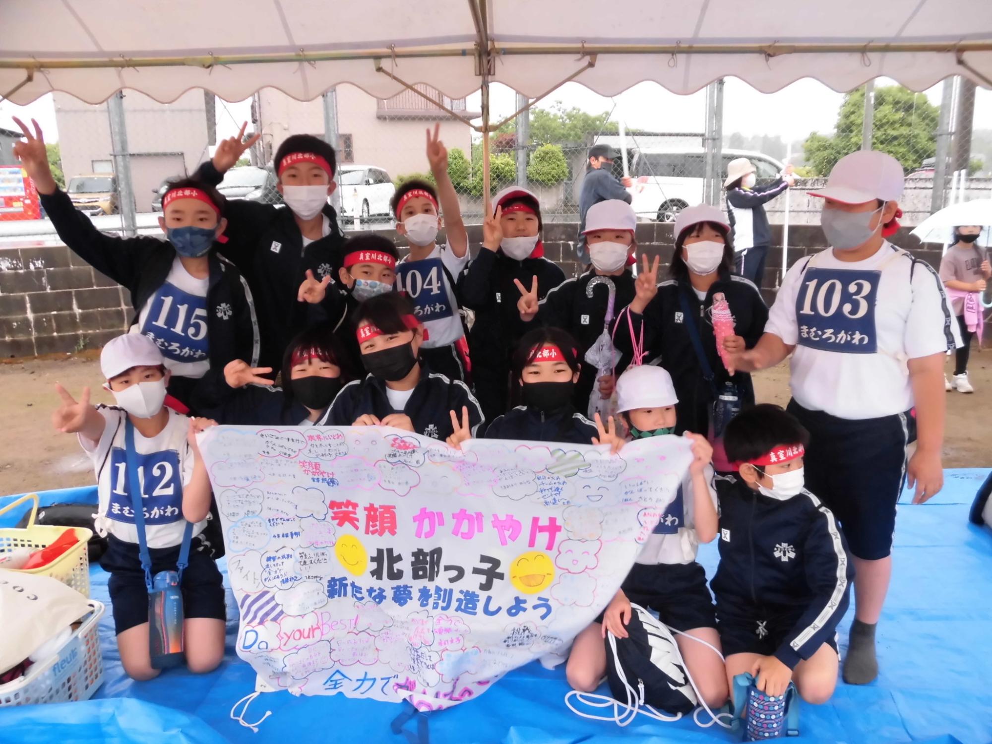 前列でしゃがみながら応援旗を掲げている児童たちと後列でピースサインをしている児童たち合計14人の集合写真