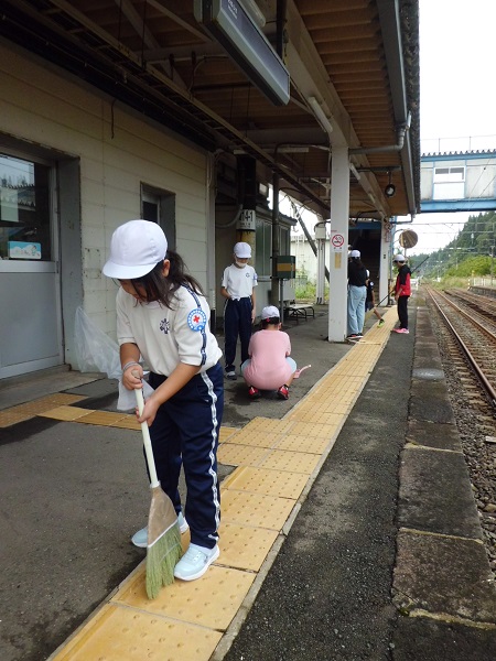 箒を持ち、駅のホームを掃除する運動帽子を被った子供たちの写真