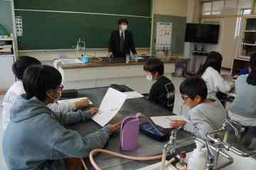 教室の壇上に立ってメダカの授業をする先生と4人グループになって真剣に話を聞く児童たちの写真