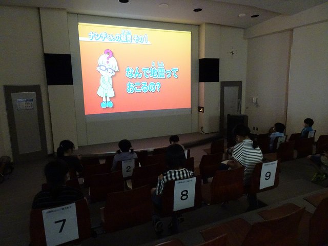 大きなスクリーンに映された災害学習の映像を熱心に見ている児童たちの写真
