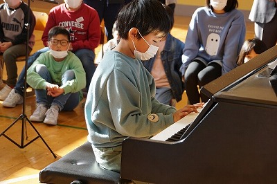 ピアノの演奏を披露する薄緑のトレーナーを着た男子児童の写真