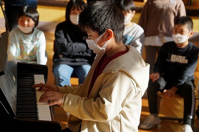 ピアノの演奏を披露するベージュのパーカーを着た男子児童の写真