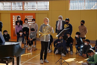 フレンチホルンの演奏を披露するグレーのトレーナーを着た男性の写真