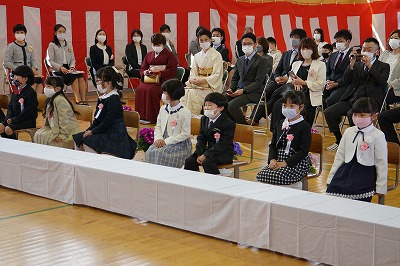着席している新入生たちと保護者たちと先生たちの写真
