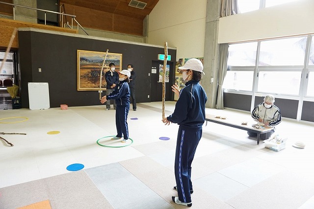 手の上に木の棒を載せ、倒れないようにバランスを取っている、2人の女子児童の写真