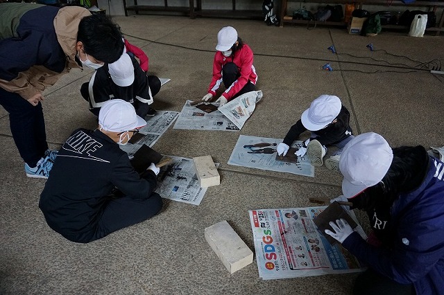 床に新聞を広げ、「焼き板クラフト」の作業を行う児童たちの写真