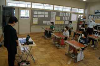 教壇に立ち講義をする新聞記者の方と着席して熱心に聴く児童たちの写真