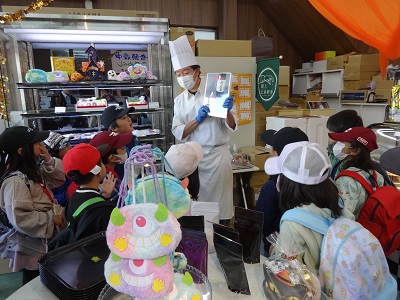 写真をもって説明しているパティシエとそれを見ている子供たちの写真