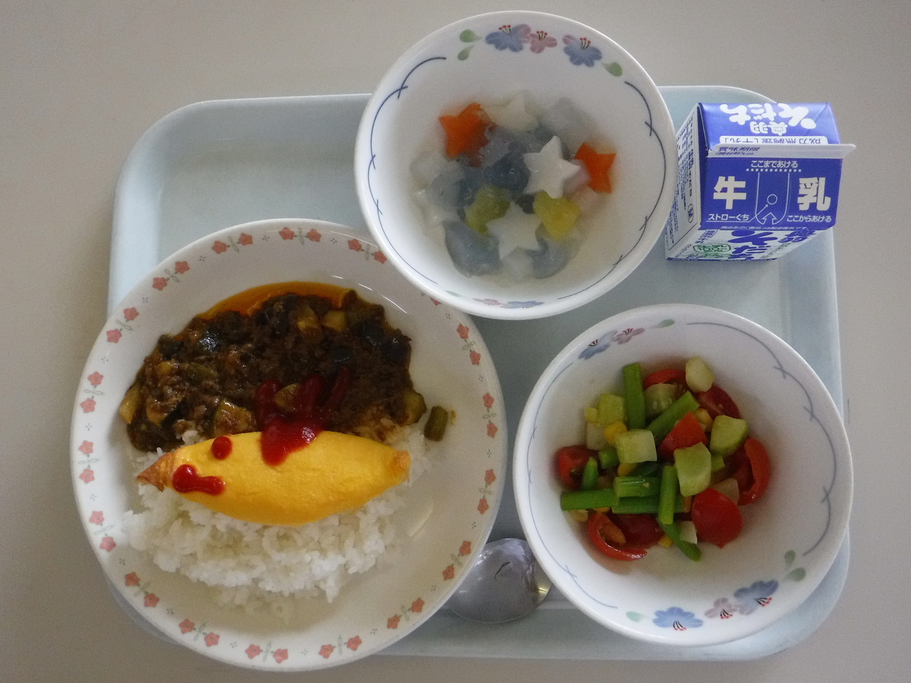 オムレツの乗ったカレーや星形に切った寒天ゼリー、サラダなどが並んでいる給食の写真
