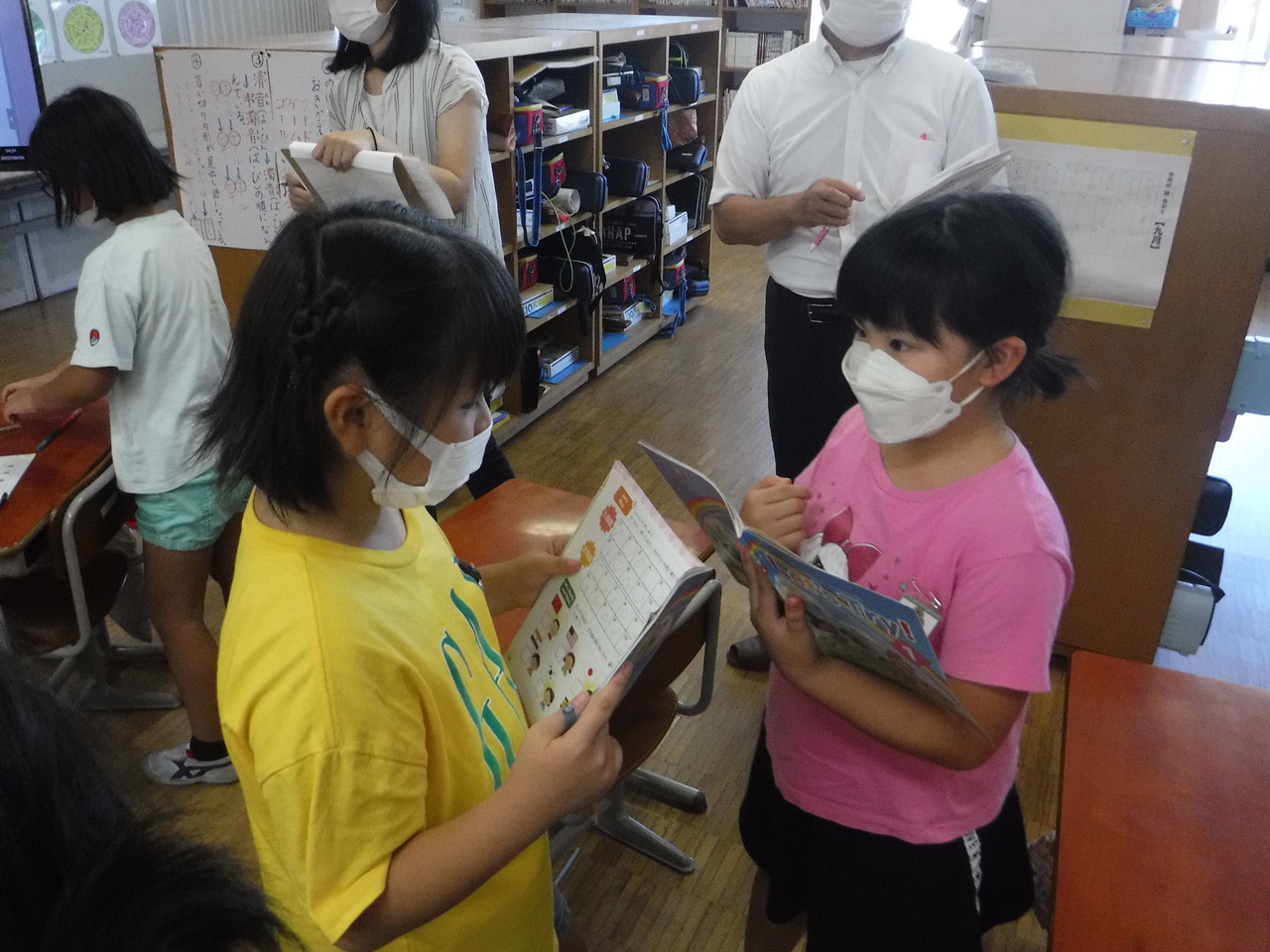 英語の教科書を手に持ちながら向かい合って会話する女の子2人の写真