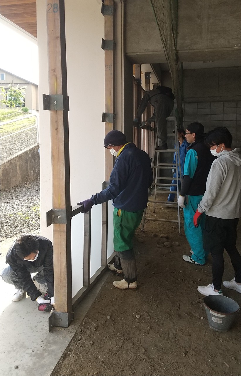 木の柱に鉄枠を設置している男性たちの写真