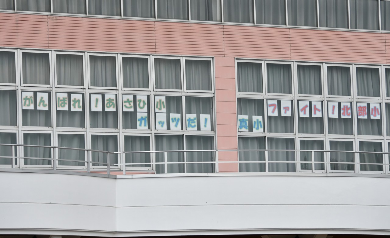 「がんばれ！あさひ小」「ガッツだ！真小」「ファイト！北部小」と書かれた紙が貼られた学校の窓ガラスの写真
