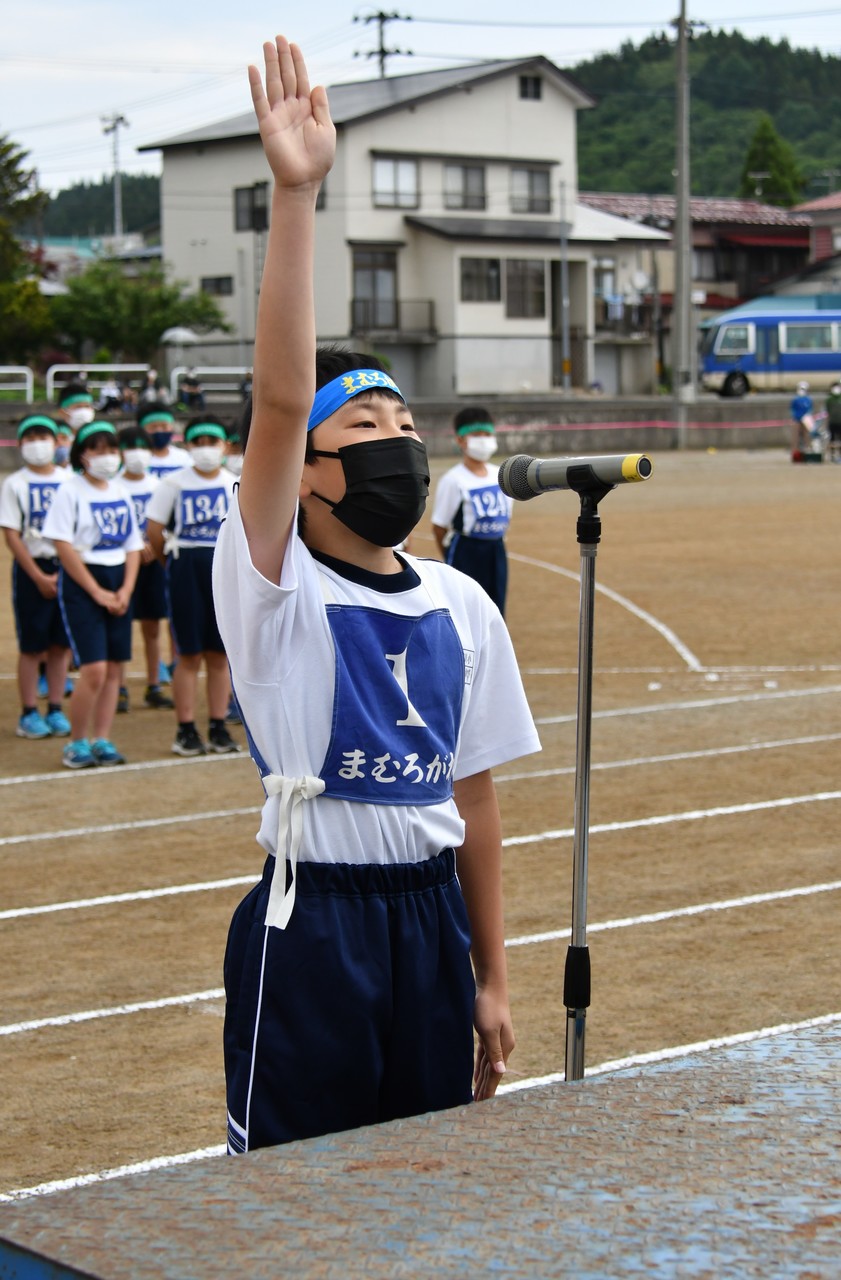 整列した子供たちの前で手を挙げてマイクに向かう体操服姿の児童の写真