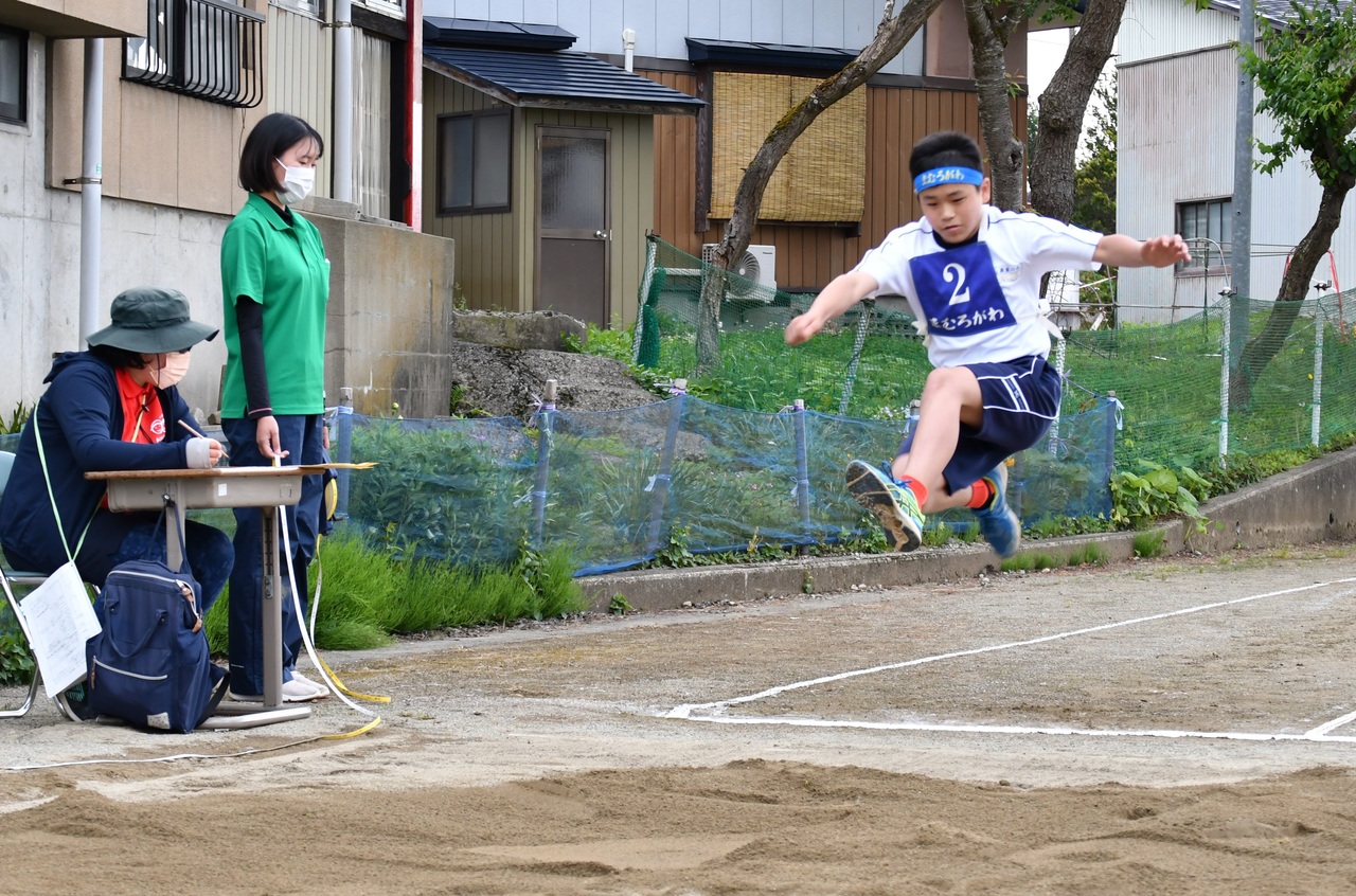 席について記録を書いている女性と、走り幅跳びで跳躍をしている少年の写真