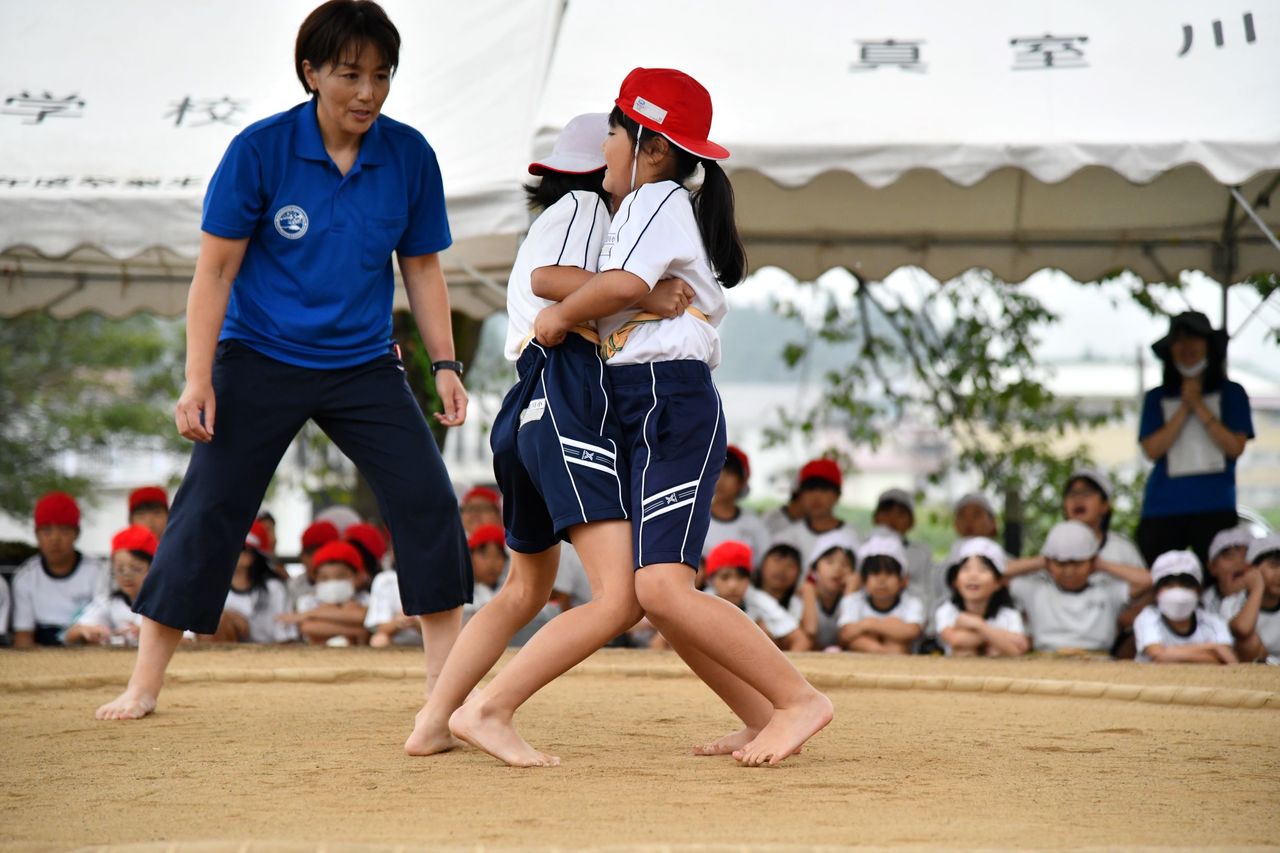服の上から身に着けたまわしを互いにつかみ合いながら押し合う二人の女子児童の写真
