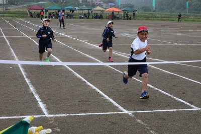 一位でゴールテープを切る男子児童と、それに続く二人の児童の写真