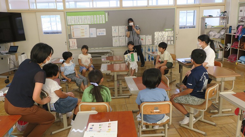 教室で中学生と一緒に輪になって座り授業を受ける2年生の児童たちの写真