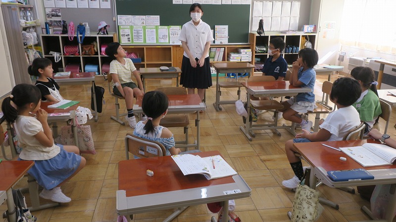 輪になって座っている児童たちの前に立ち挨拶をする中学生の写真