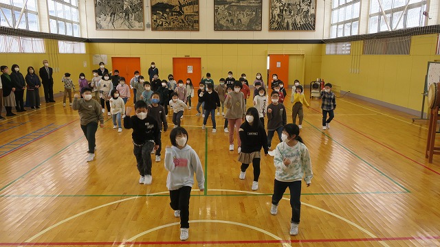 体育館に集まってダンスを披露する、1～4年生の児童たちの写真