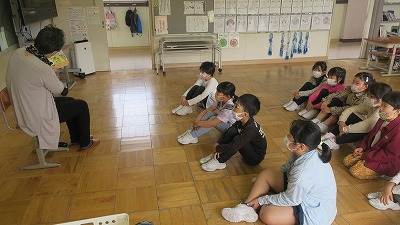 床に座って読み聞かせに聞き入る児童たちの写真