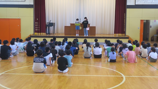 2人の児童代表が壇上に立ち2学期の挑戦について発表し、それを座って聞いている児童たちの写真