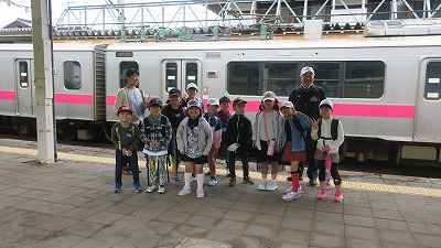 校外学習にて、JR真室川町駅のホームで、向かいに停車している電車を背景に撮影された、教職員の男女2人と、2年生の児童11人の集合写真