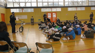 学校の体育館で前に立って話す男性と座って聞く子供たちの写真