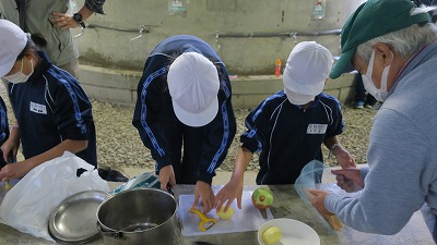 鍋の前で野菜の下ごしらえをする、体操着姿の児童たちの写真