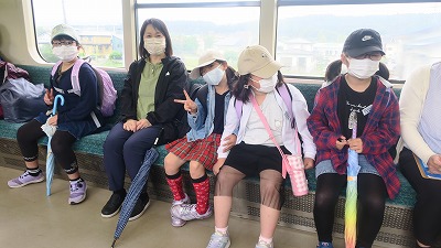 校外学習にて、電車内のシートにリラックスした様子で座る、2年生の女子児童達の様子を写した写真