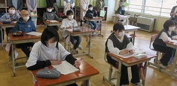 授業に聴き入る児童たちと、それを背後からあたたかく見守る保護者の方たちの写真