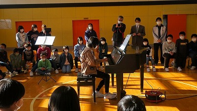 ピアノの演奏を披露する薄紫のパーカーを着た女子児童を、少し遠くから撮った写真