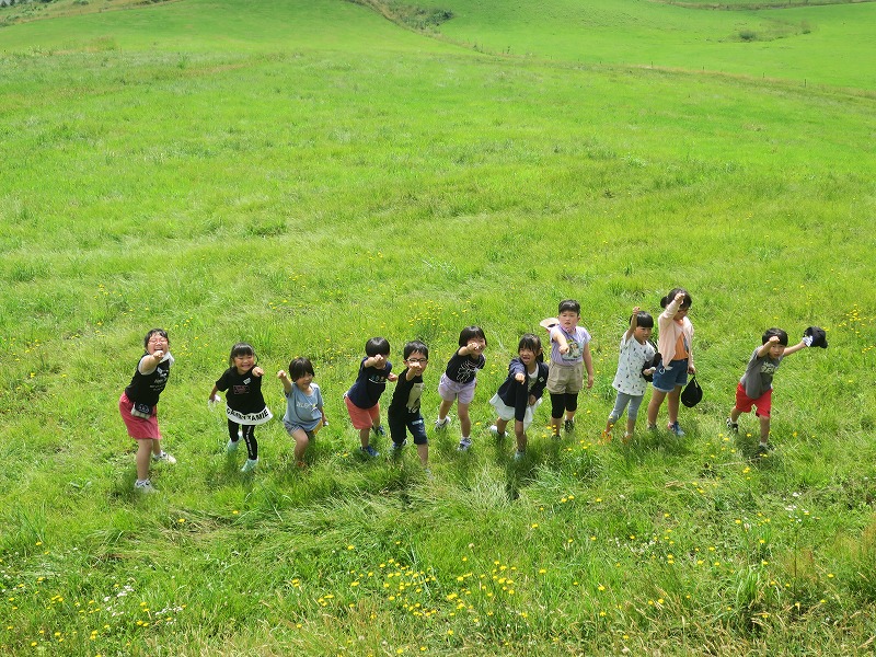 緑一面の牧草地でこぶしを突きあげてポーズをきめる児童たちの写真