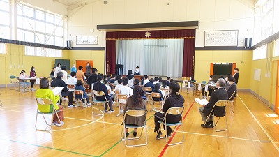 立って話す男の子と座って聞く児童たちと先生たちの写真