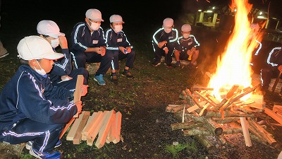 勢いよく燃え上がるキャンプファイアーの光に照らされた児童たちの写真