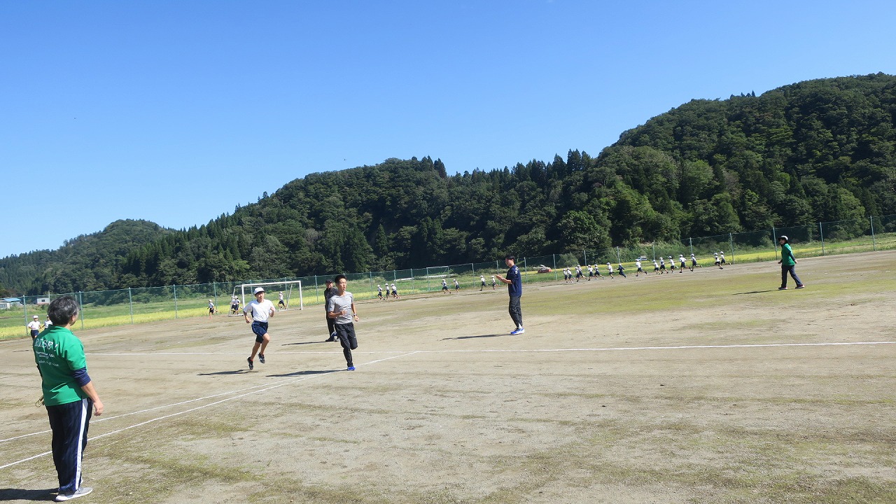運動場を1周する間、駅伝選手に伴走されながら走る高学年の児童たちの写真