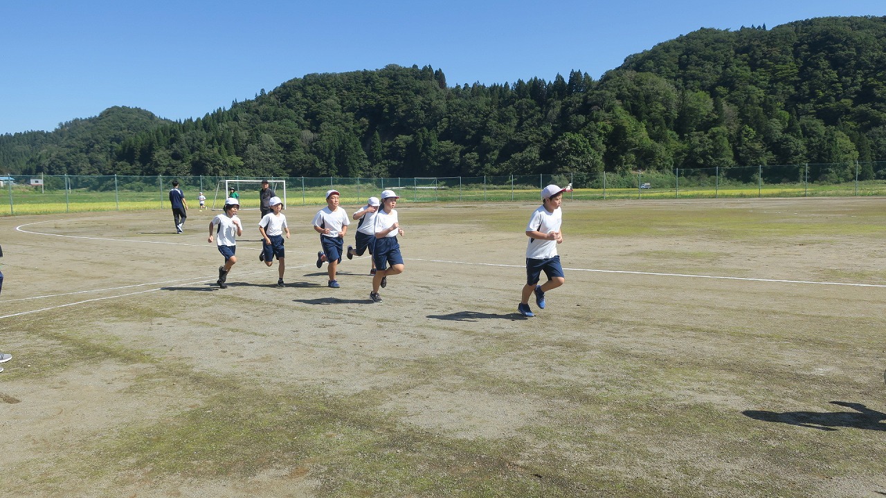 運動場を1周し学校敷地外のコースに向かって走る高学年の児童たちの写真