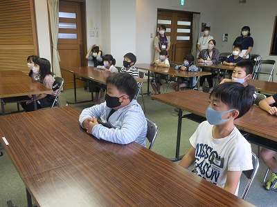 会議用テーブルの前に座って、読み聞かせを熱心に聴く児童たちの写真