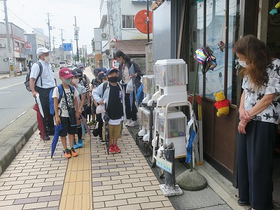 駄菓子屋のおばさんに見送られて昼食の場所に向かう児童たちの写真