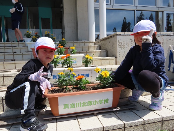 階段に置かれた「真室川北部小学校」と書かれた紙の貼られたプランターの横にしゃがみ、ピースをする2人の子供の写真
