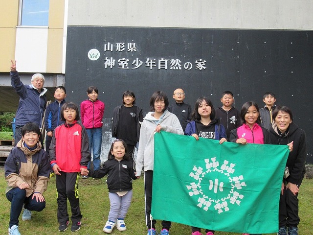 「神室少年自然の家」の前に集合し、緑の旗を広げてポーズをとる児童たちの写真