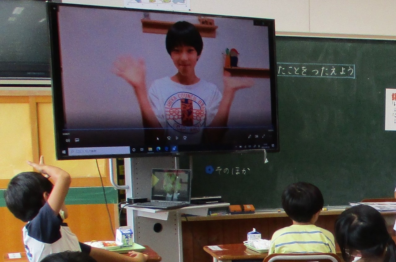 手を振る少年が映ったモニターを眺める子供たちの写真
