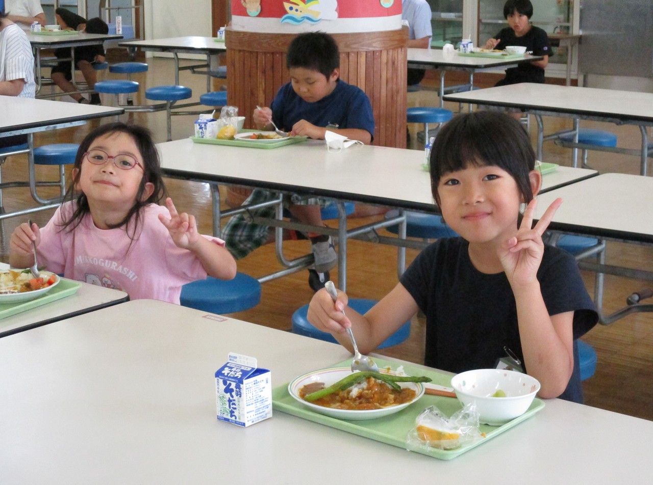 カレーを食べながらカメラ目線でピースをする二人の子供の写真