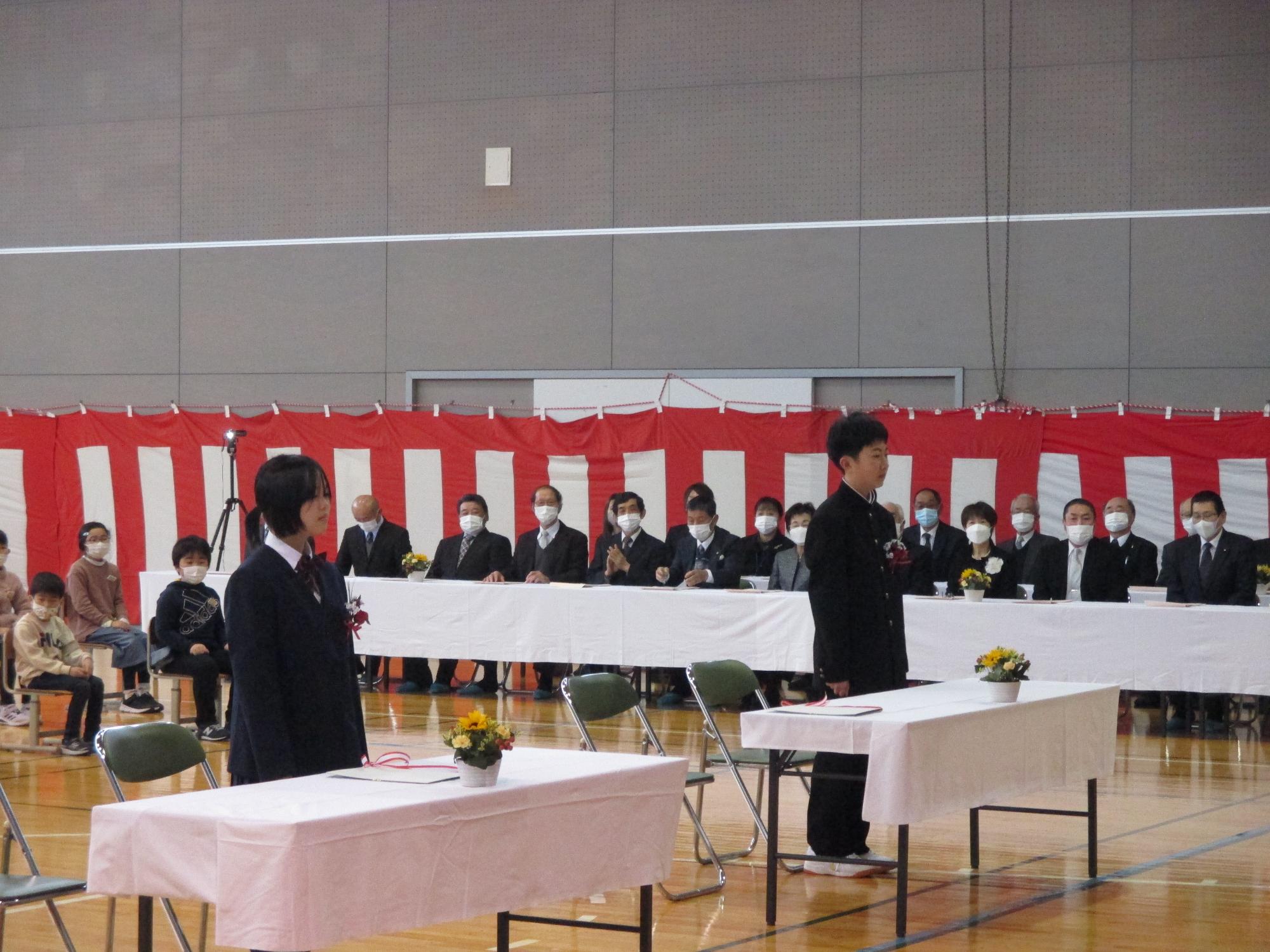 男女の卒業生が、並んで体育館の正面を向いている写真