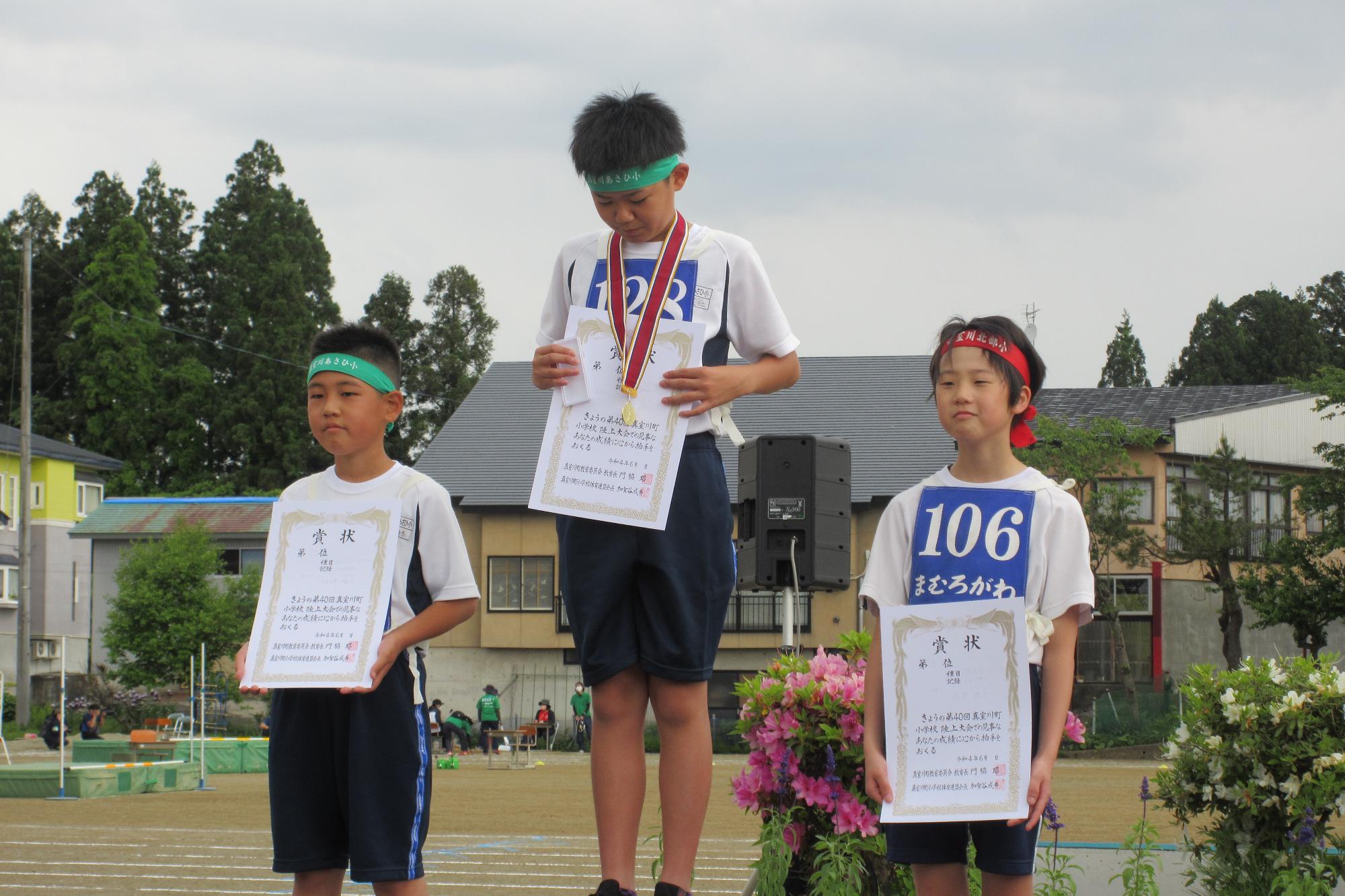 表彰台に上がった1位の男子児童が首にかけられたメダルを眺めている様子の写真