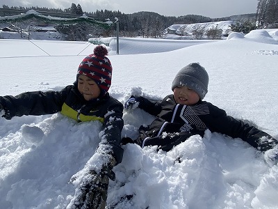 雪の中に下半身を埋もれさせ、雪の温泉に浸かる2人の生徒の写真