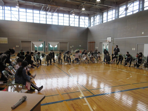 体育館にて円状にパイプ椅子に座っている生徒たちの写真