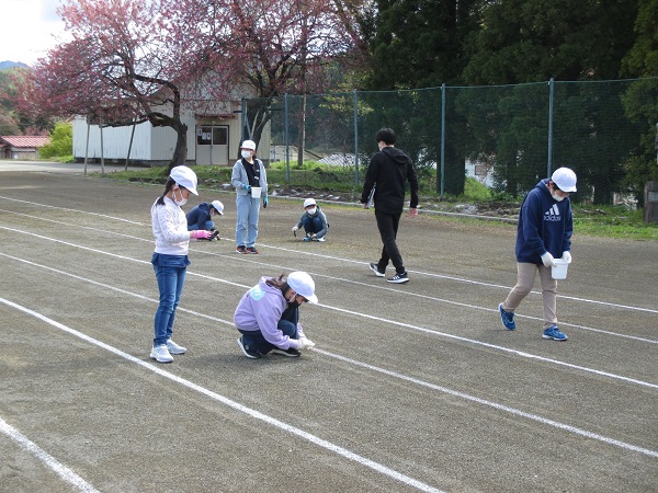 グランドの白線の上で白帽子を被った子供たちがしゃがみこんでいる写真