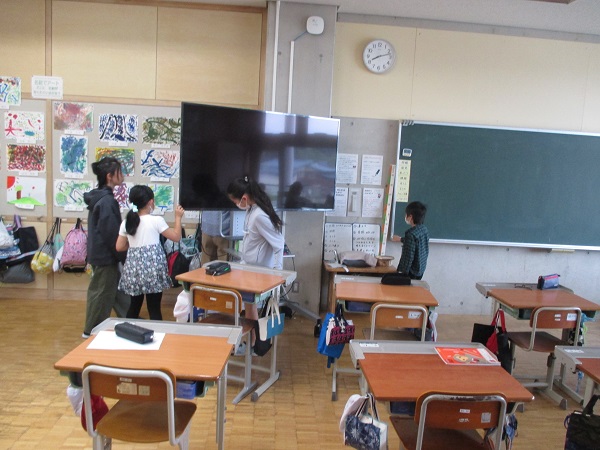 教室のモニターの裏側を見る子供たちの写真