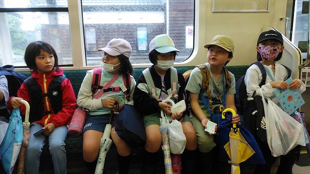 傘をきちんとたたみ、行儀よく電車の席におさまる児童たちの写真